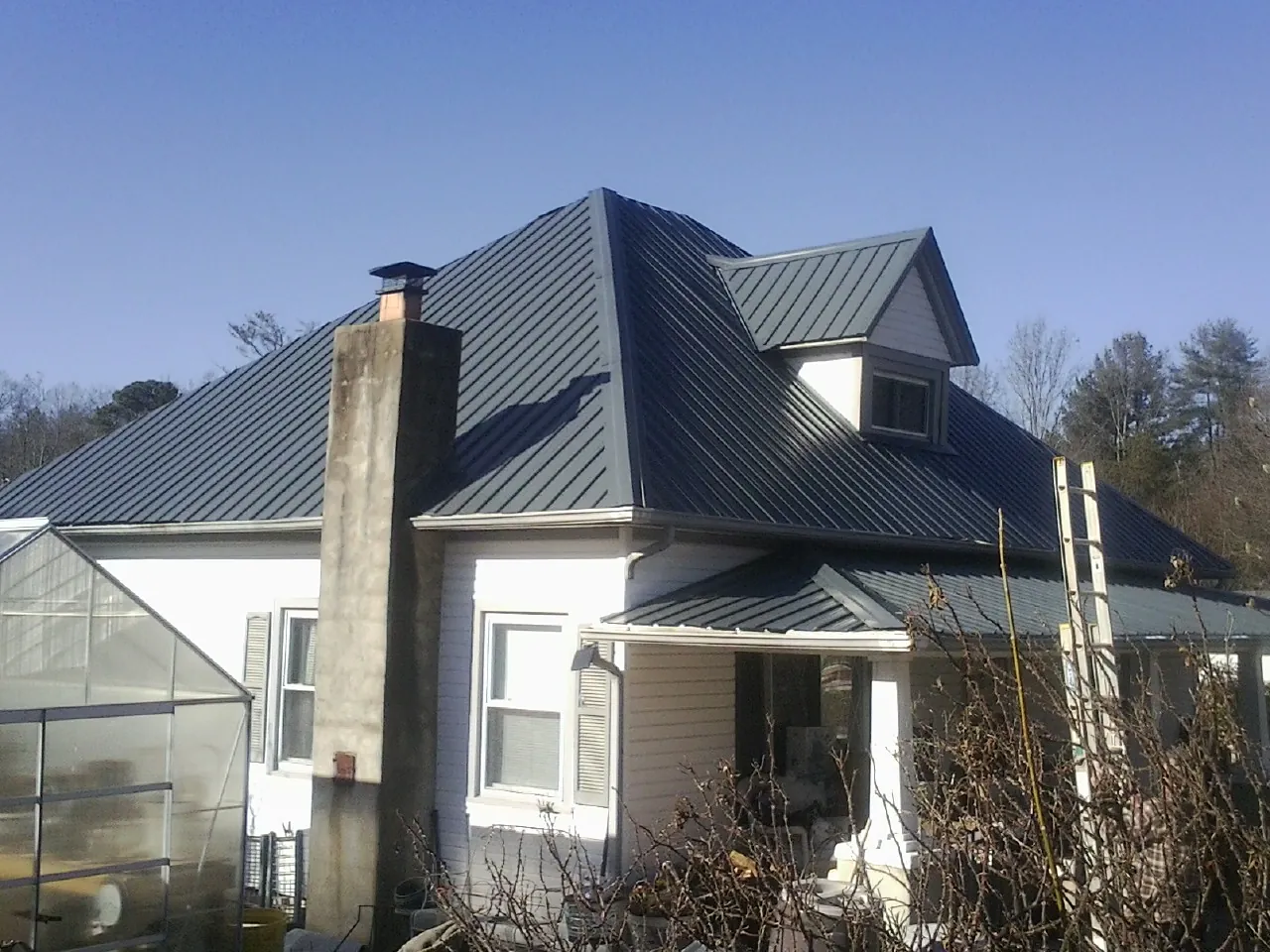 Dark blue standing seam metal roof on a white farmhouse with dormer — Slate & Tile Roof Repair by Roofing Brothers in Paola