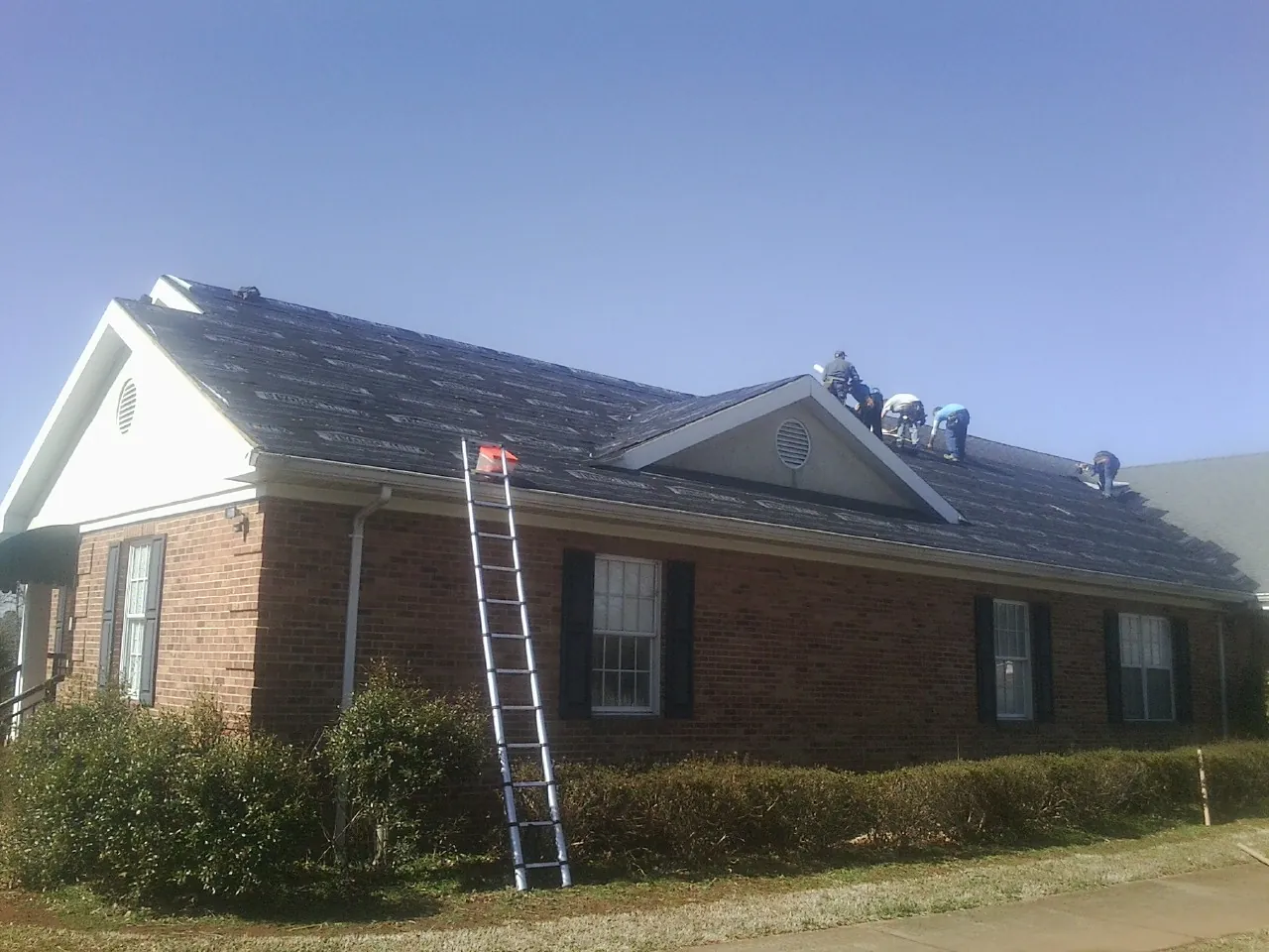 Crew tearing shingles off a brick ranch roof with a ladder set — Emergency Roof Repair work by our crew in Paola