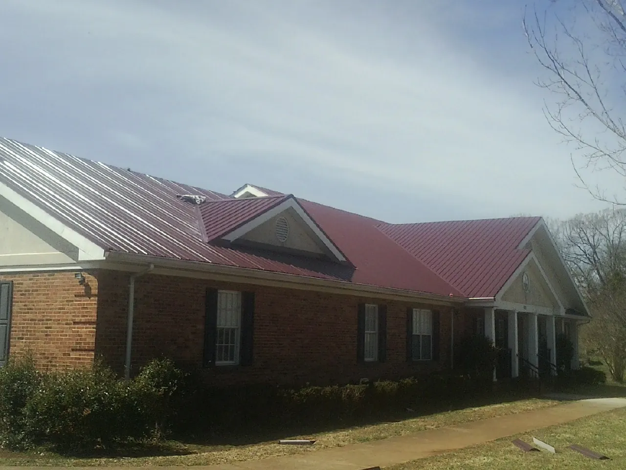 Red metal roof with gabled entries on a long brick building, from a Hail Damage Roof Repair job in Paola