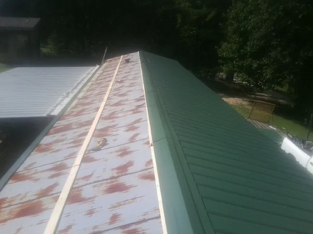 Old rusted panels beside newly installed green metal roofing — Wind Damage Roof Repair by Roofing Brothers in Paola