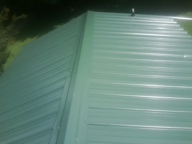 New green metal panels meeting at the ridge of a roof — Flat Roof Repair work by our crew in Paola