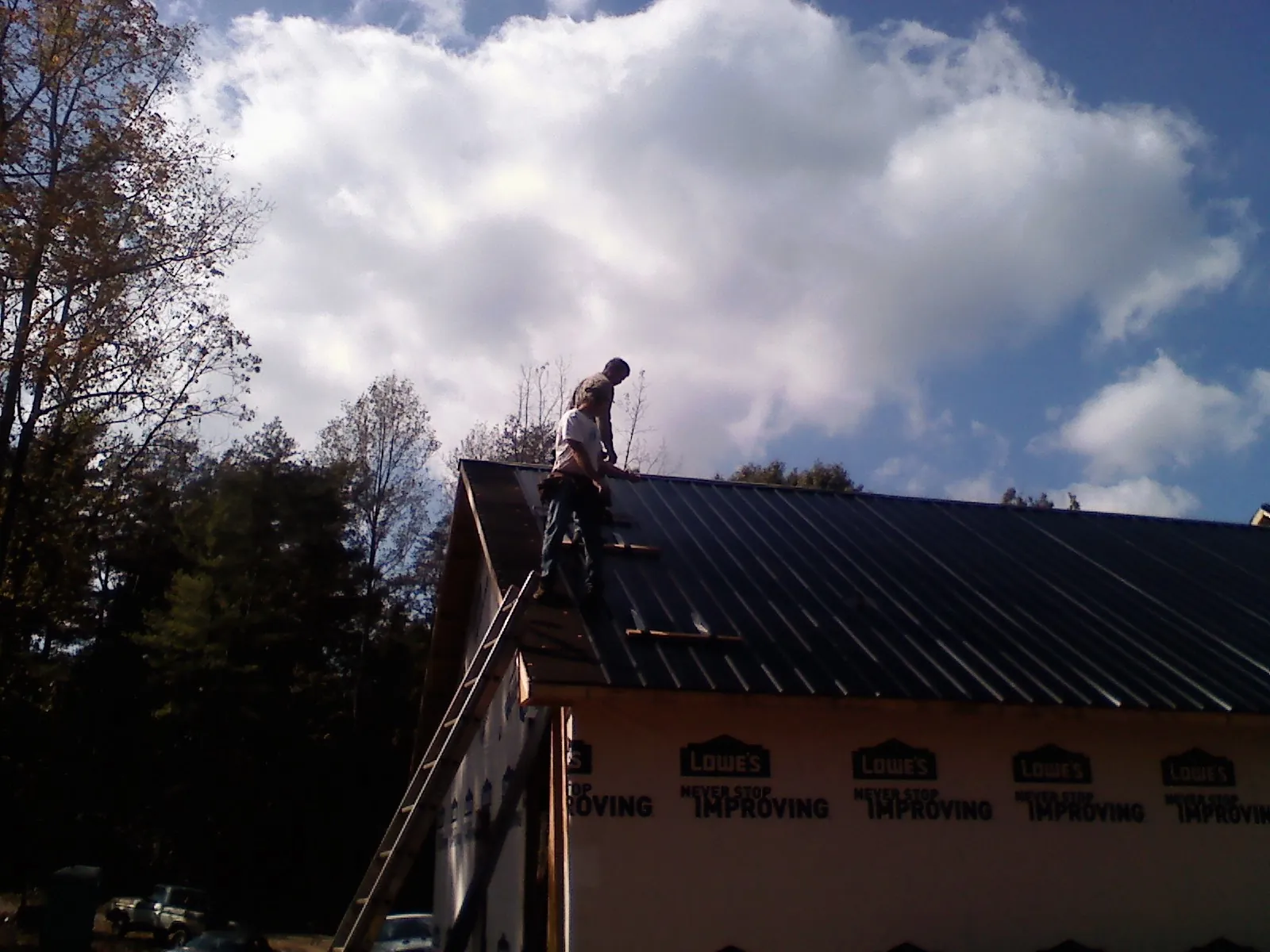 Roofer fastening dark metal panels high against a cloudy sky, from a Roof Inspection job in Paola