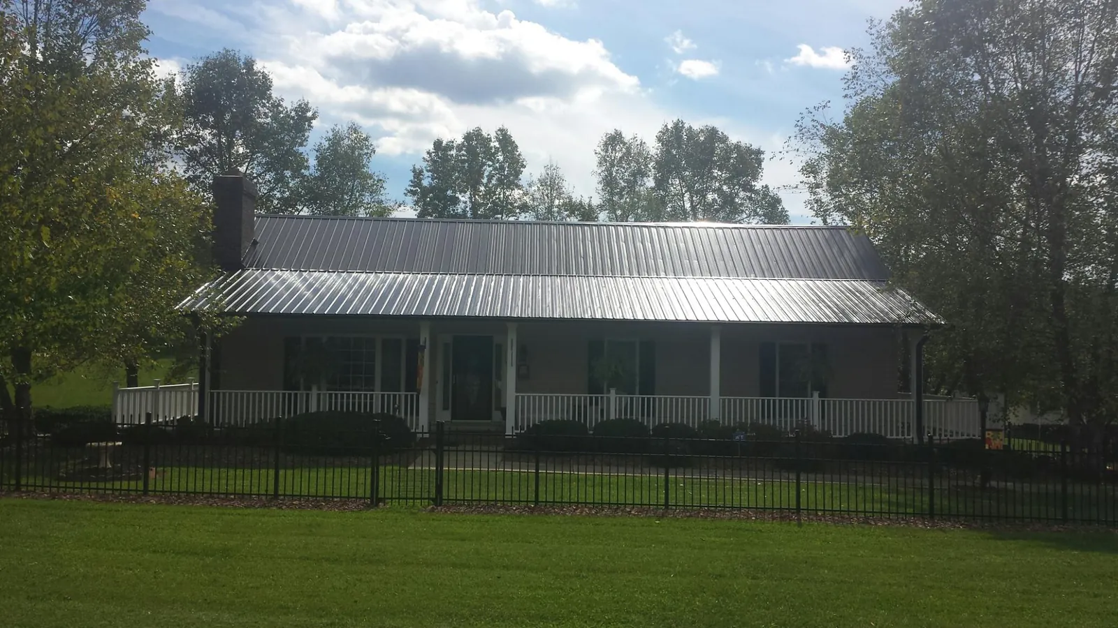 Gray metal roof on a brick ranch with a full width front porch — Gutter Guard Installation work by our crew in Paola