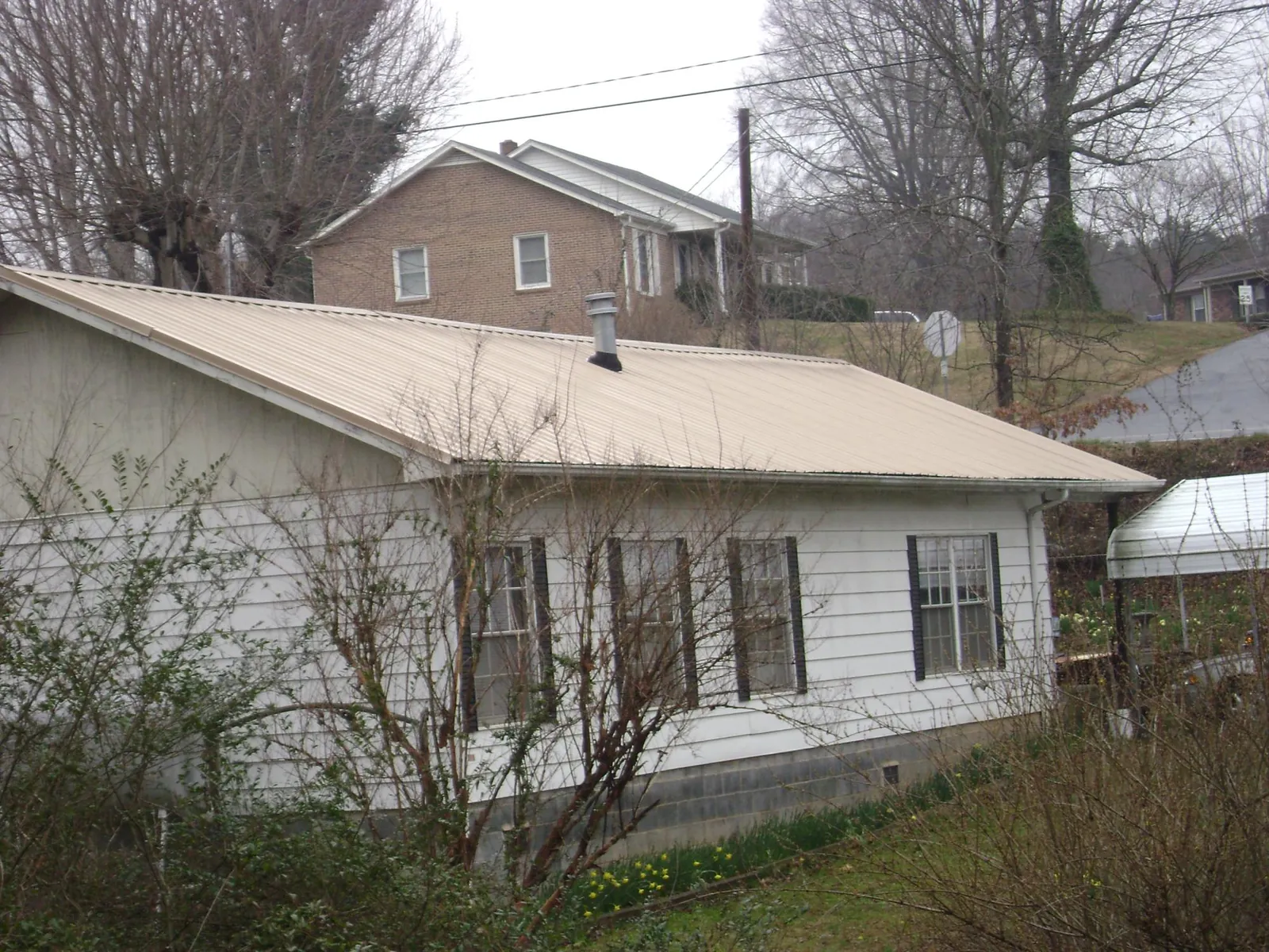 Tan metal roof on a white sided house set into a hillside — Commercial Roofing by Roofing Brothers in Paola