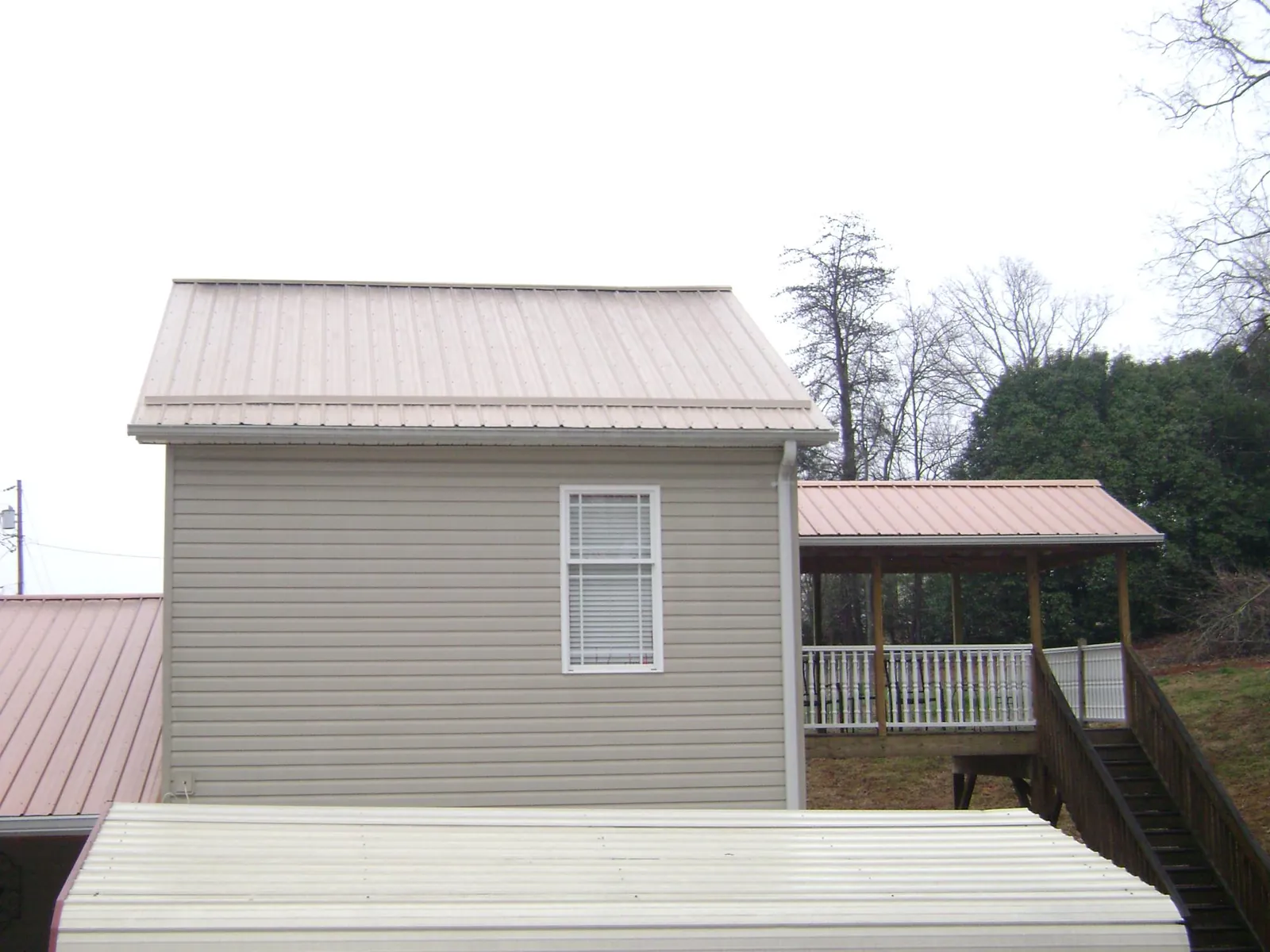 Tan metal roofs on a two story addition and attached porch, from a Roof Replacement job in Paola